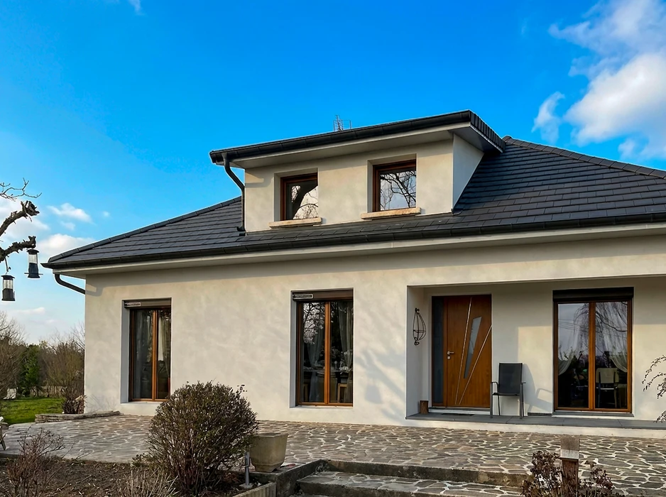 Maison individuelle moderne, vue extérieure de façade, enduit blanc lisse, toiture à quatre pans en tuiles ardoisées anthracite avec lucarne centrale