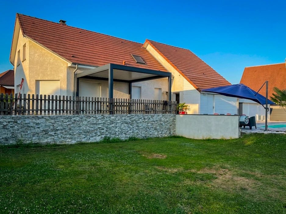 Pergola bioclimatique autoportante en aluminium anthracite, installée sur une terrasse en composite imitation bois