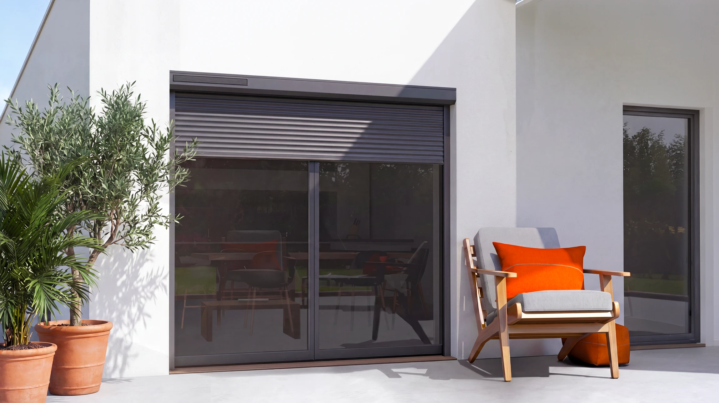 Maison résidentielle moderne avec volets roulants solaires gris ou blancs installés sur les fenêtres en façade, vue extérieure de jour montrant clairement les volets fermés ou semi-fermés sur plusieurs baies vitrées, avec un petit panneau solaire visible intégré au système de volet en haut de baie ou en discret sur toiture, environnement résidentiel calme et végétalisé